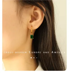 Detail of model wearing 18K gold-plated earrings with rectangular green gemstone drops