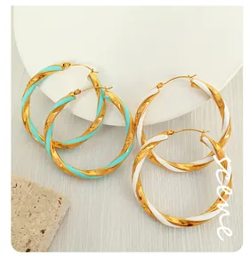 Dettaglio di grandi orecchini a cerchio dorati a spirale con smalto blu e bianco lucido