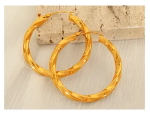 Detail view of gold-plated twisted hoop earrings on beige stone and fabric background