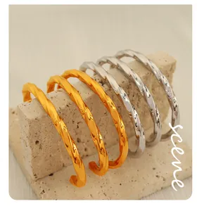 Polished gold and silver twisted cuff bracelets displayed on a stone prop texture