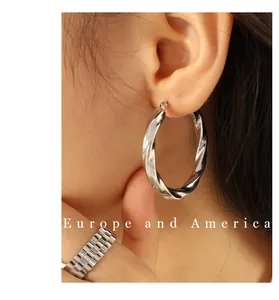 Close-up of chunky silver-colored twisted hoop earrings and wide texture metal ring