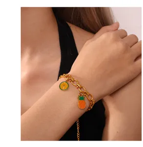 Detail of a gold chain bracelet featuring vibrant enamel orange and pineapple fruit charms
