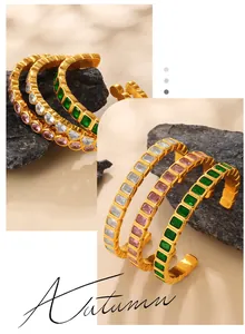 Detailed view of C-shaped gold cuff bracelets with colorful zircon stones and brushed texture