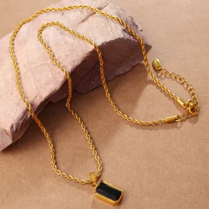 Golden twist chain necklace with a rectangular black gemstone pendant on a rustic rock