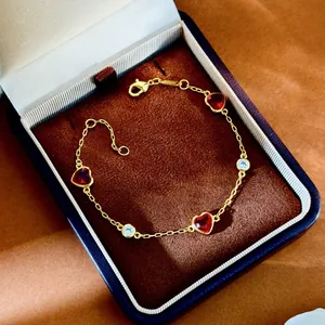 Détail d'un bracelet doré avec pierres en cœur rouges et zircons dans un écrin en velours