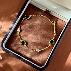Détail du bracelet doré avec pierres de cœur vertes et zircons dans un coffret cadeau