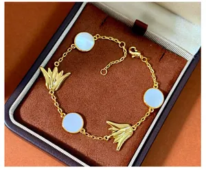 Nahaufnahme eines goldenen Armbands mit weißen Muschelscheiben und Lilienblütenanhängern