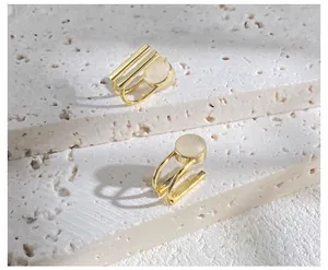 Macro detail of asymmetric gold ear clips with white cat eye stones on stone texture