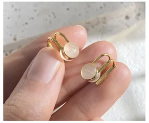 Close-up of asymmetrical cat eye stone clip earrings with polished gold finish