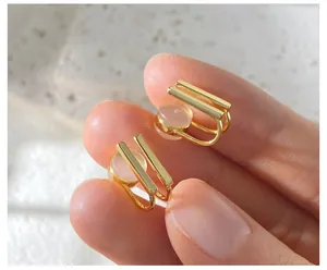 Detailed view of gold geometric cat eye ear cuffs held between fingers showing fine texture