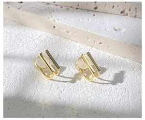 Close-up of golden geometric clip-on earrings with white cat-eye stone on stone surface