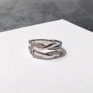 Crossed silver U-shaped ring with pavé micro-inlaid diamonds on a gray stone surface