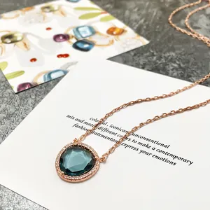 Détail d'un collier en or rose avec une grosse pierre bleue en goutte et un halo de zircons