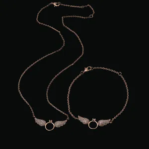 Rose gold angel wing necklace and bracelet set with sparkling diamonds on black background