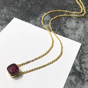 Détail d'un collier doré avec pendentif carré alvéolé serti de pierres rouges