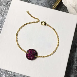 Détail macro du bracelet à chaîne dorée avec pendentif rond orné de strass roses brillants