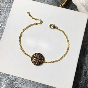 Vue détaillée du bracelet en chaîne dorée avec pendentif rond pavé de cristaux bruns