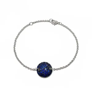 Détail du bracelet en chaîne argentée avec breloque ronde pavée de pierres bleues et fermoir