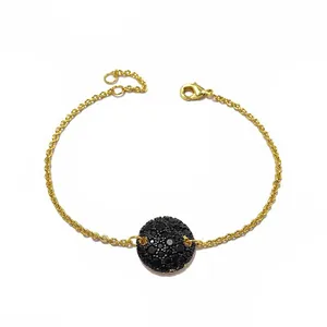 Détail du bracelet doré avec pendentif disque pavé noir et chaîne à fermoir ajustable