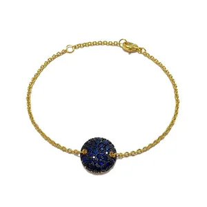 Détail du bracelet en chaîne dorée avec pendentif rond serti de cristaux bleus