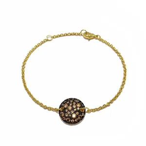 Détail d'un bracelet doré avec un pendentif rond serti de zircons marron scintillants