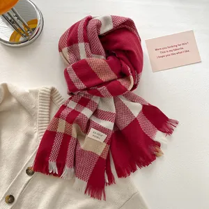 Detail of red and white plaid wool scarf featuring fringe edges and brand label