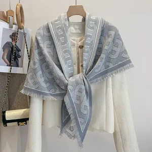 Detail eines weichen grau-weißen Schals mit Quasten über einer Tweed-Jacke