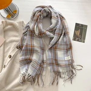 Detail of soft blue and orange checkered scarf with fringe and brand label on knit background