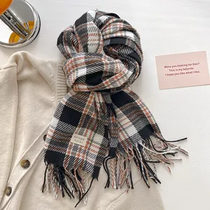 Detail view of plaid scarf with orange accents, fringe edges and a minimalist logo label
