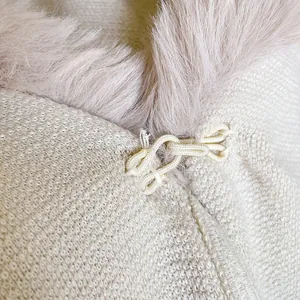 Detail of faux rabbit fur collar and knot buckle on beige knitted oversized poncho