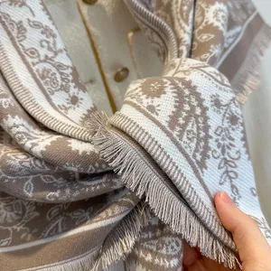 Detailed macro view of the paisley jacquard texture and fringes on this beige scarf