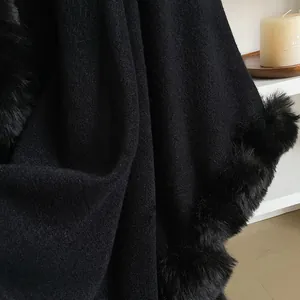 Close-up of black oversized poncho with faux rabbit fur trim and thick wool texture