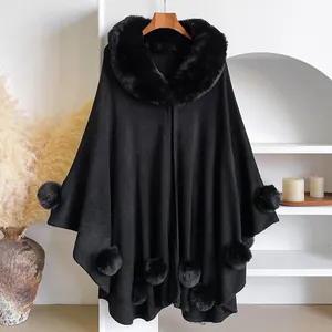 Detail of black knit poncho featuring a plush faux fur collar and decorative pom-poms