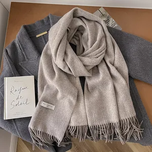 Detail of oatmeal wool scarf with tassels on dark coat showcasing soft winter texture