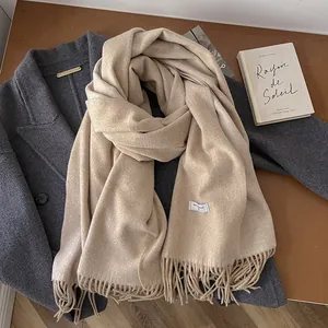 Detail of beige wool scarf with fringe trim styled on a grey coat with a book