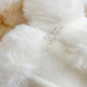 Detail of white knit cloak featuring plush faux fur trim and handcrafted braided button