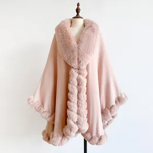 Detail of light pink knitted poncho featuring soft faux fur trim and pom-pom fastener