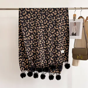 Détail d'une écharpe léopard avec franges à pompons noirs et étiquette tissée
