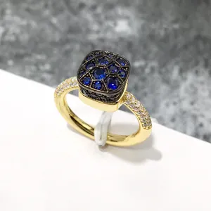 Detalle de anillo dorado cuadrado con gemas azules y micro-pavé de circonitas blancas