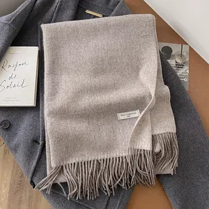 Minimalist oatmeal wool scarf with tassels, draped over a dark grey winter coat