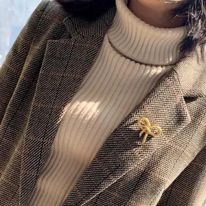 Golden bow brooch with twisted metal texture pinned on a brown plaid blazer lapel