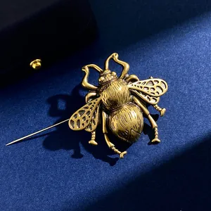 Macro shot of vintage golden bee brooch with hollow wings on dark blue fabric texture