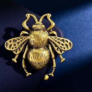 Macro detail of antique gold bee brooch featuring hollowed wings on dark blue silk