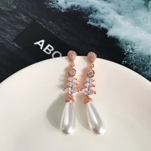 Dettaglio di orecchini lunghi con perle oro rosa e cristalli su un piatto di porcellana