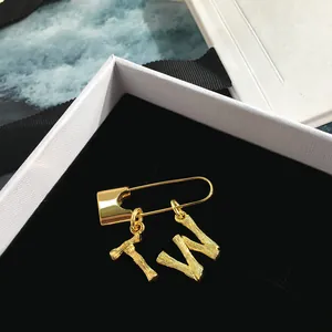 Golden safety pin brooch with bamboo textured letters T and W on black velvet