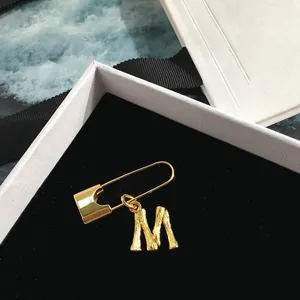 Close-up of golden bamboo texture letter M pendant on a safety pin brooch in a gift box