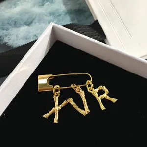 Detail of gold safety pin brooch with XVR bamboo texture letter charms in a gift box