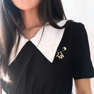 Close-up of golden alphabet brooch with T and W charms on a black and white dress