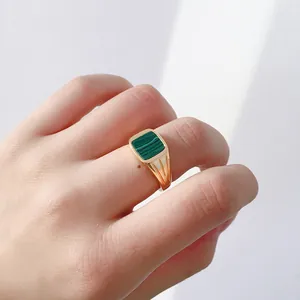 Détail d'une bague chevalière carrée en or avec pierre de malachite sur le doigt