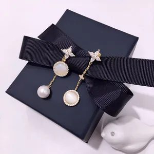 Detail of asymmetrical gold earrings with marquise stones and natural pearl in a gift box